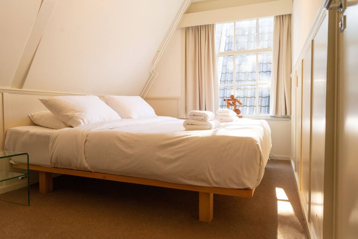 A bedroom with a bed, a glass side table, and a window with curtains.