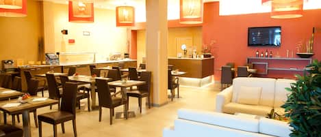 A hotel lobby with dining tables, chairs, a reception desk, and a TV screen.