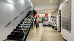 A modern interior with a glass staircase, a reception desk, and a wall-mounted directory. - Hotel Sercotel Portales (Logroño)