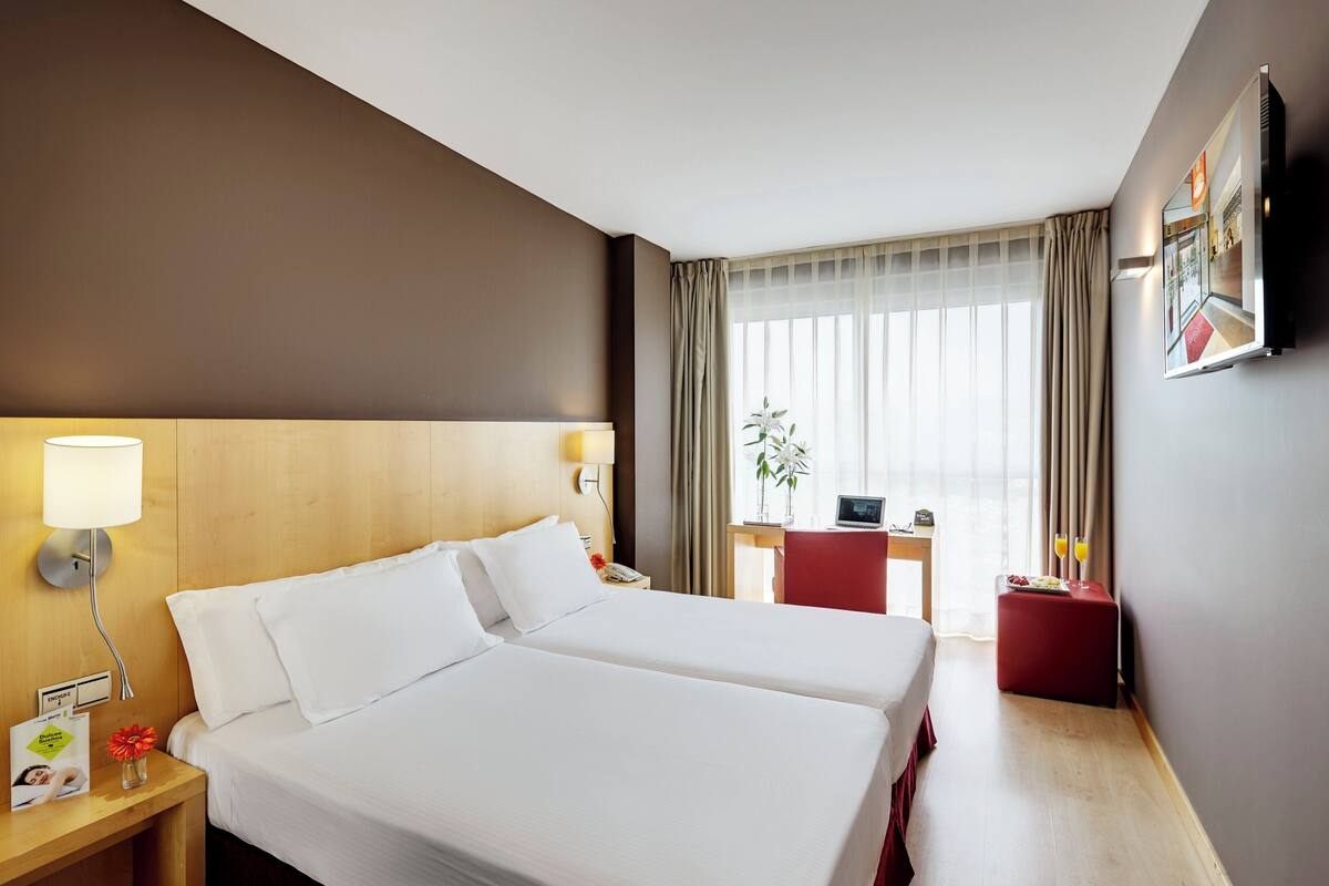 Une chambre d’hôtel avec deux lits, un bureau, une chaise, une télévision et une fenêtre avec des rideaux.