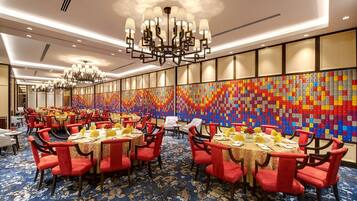 A hotel dining area with round tables, red chairs, and a colorful wall art installation.