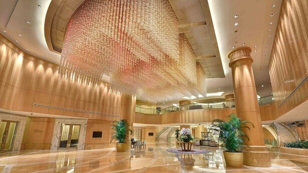 Un hall espacioso con una gran instalación floral circular suspendida, suelos de mármol pulido y una imponente escalera.