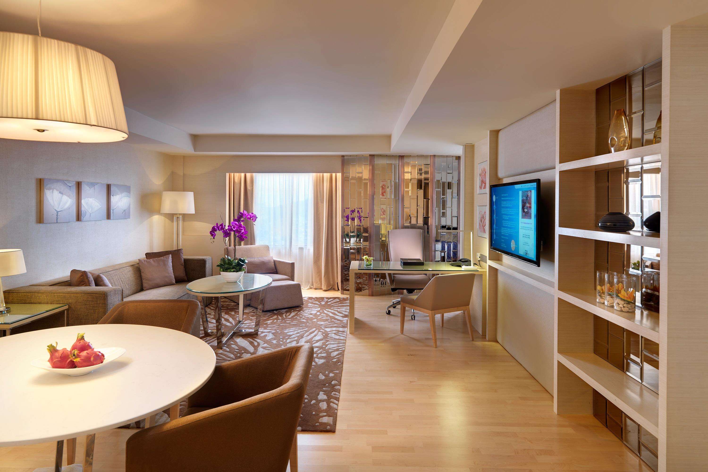 A modern hotel room with a dining area, a living room, a workspace, and a television.