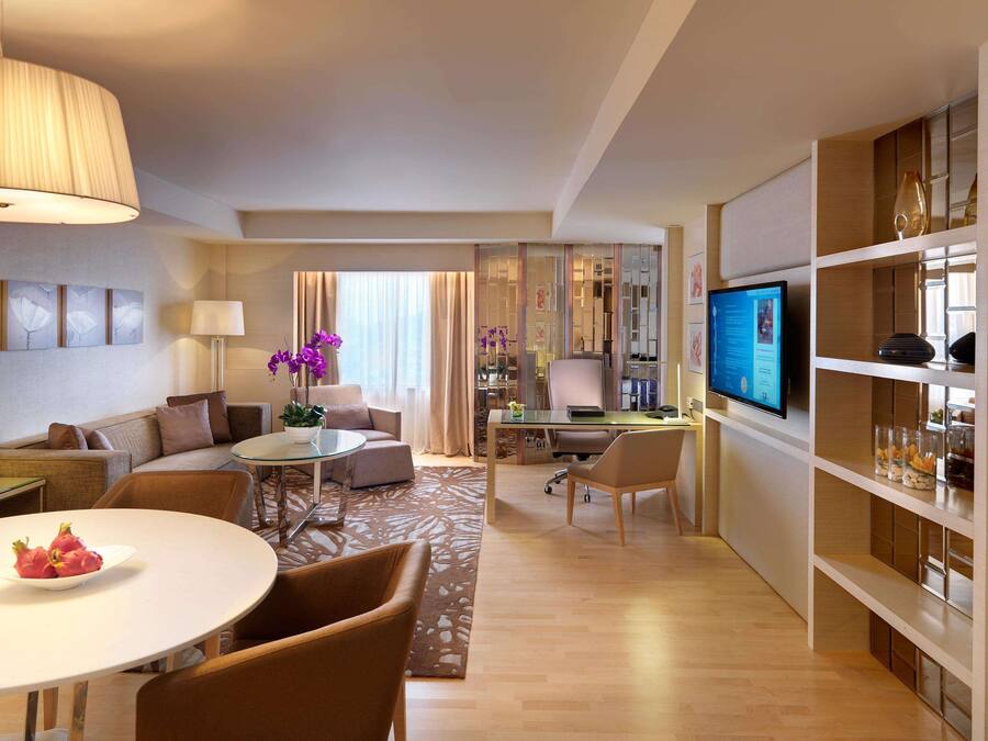 Una habitación de hotel moderna con comedor, sala de estar, espacio de trabajo y televisor.