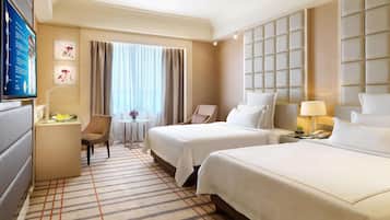 A hotel room with two beds, a desk, a chair, a TV, and a window with curtains.