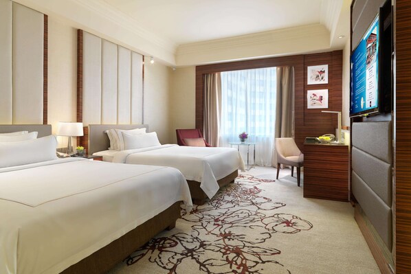 A hotel room with two beds, a desk, a chair, a television, and a large window with curtains.