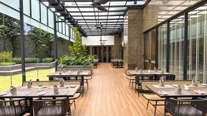 Un restaurante moderno con suelo de madera, mobiliario negro y de mimbre, y techo de cristal.