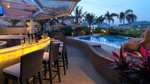 Zona de bar al aire libre con piscina, taburetes y sombrillas.