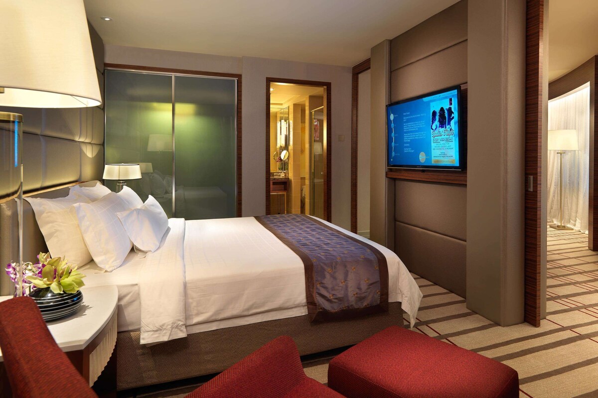 Habitación de hotel con una cama, televisor, escritorio con lámpara y una silla roja.