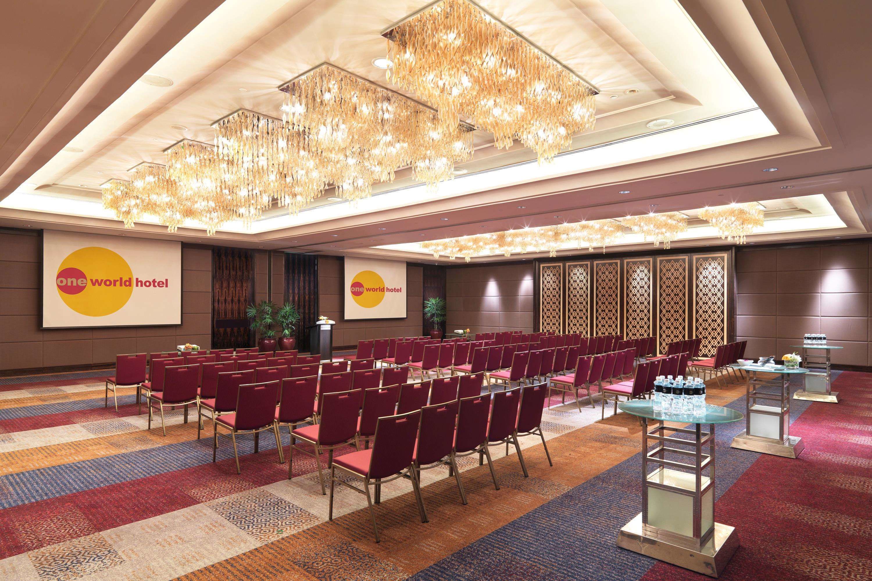 A conference room with rows of red chairs, a large chandelier, and a 'one world hotel' sign.
