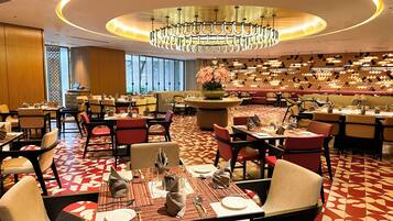 A restaurant with round tables, red and white patterned flooring, and a central chandelier.
