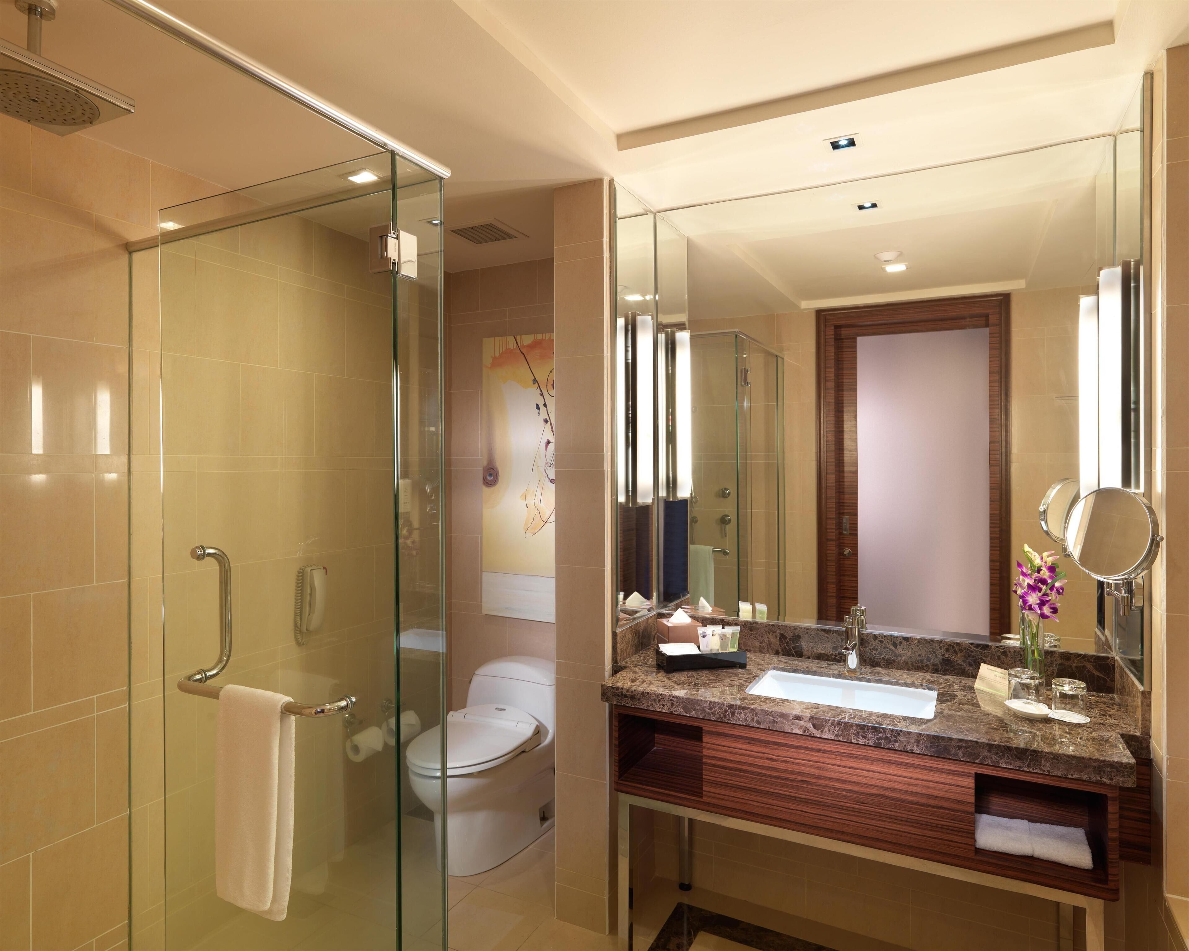 A modern bathroom with a glass shower enclosure, a toilet, a sink with a marble countertop, and a large mirror.