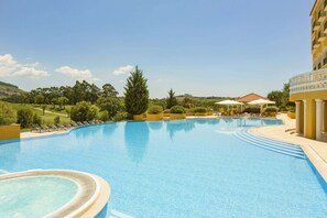 A large, curved swimming pool with lounge chairs and umbrellas, surrounded by greenery and a building with balconies. - Dolce by Wyndham CampoReal Lisboa (Torres Vedras)