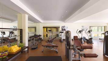 Un gimnasio amplio con diversos equipos de ejercicio, un espejo grande y un cuenco con fruta.