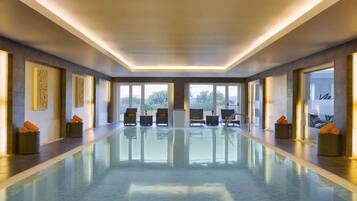 Una larga piscina interior de diseño moderno, con un pasillo central y zonas de estar con cojines naranja.
