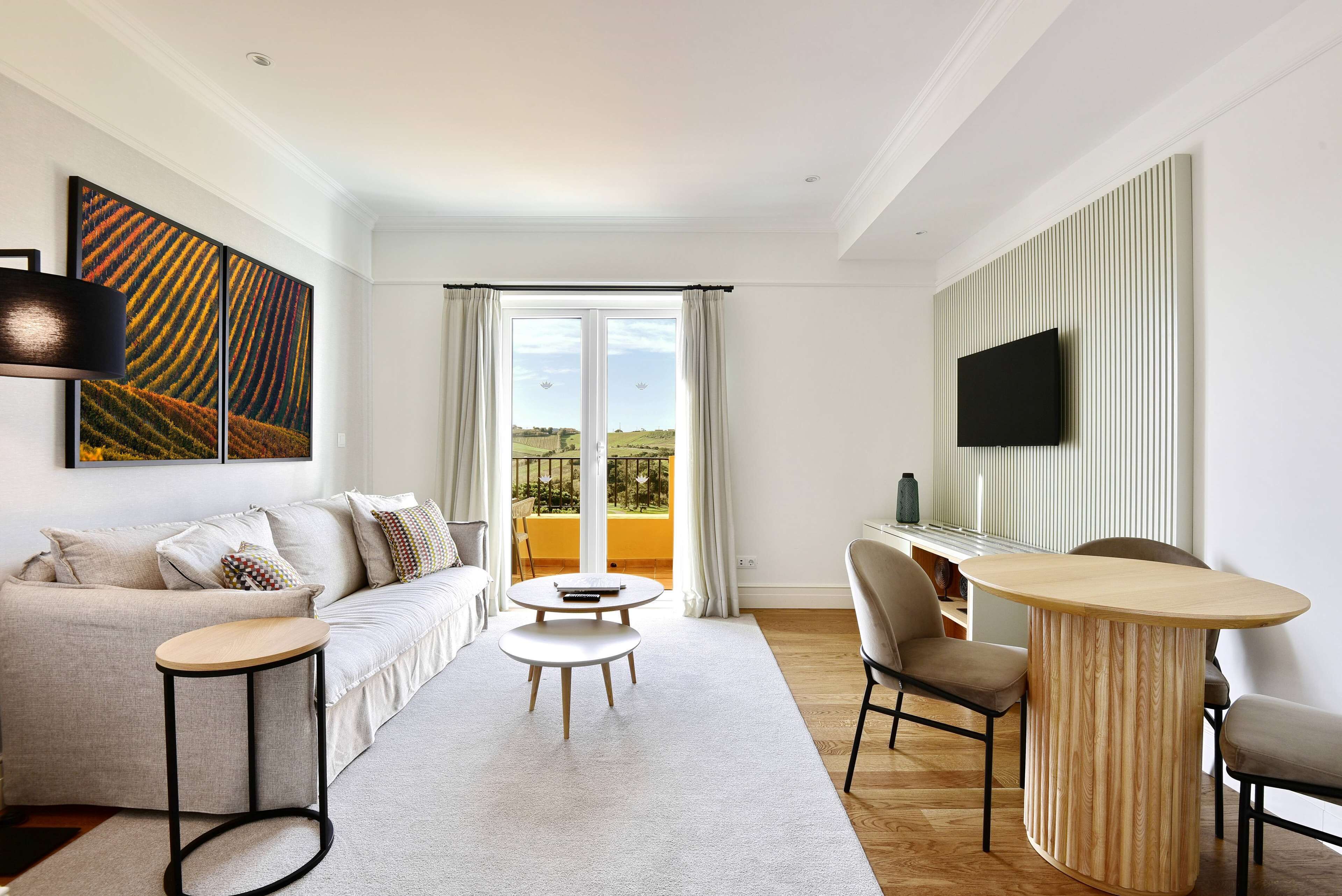A modern living room with a sofa, two side tables, a coffee table, a TV, and a balcony with curtains.