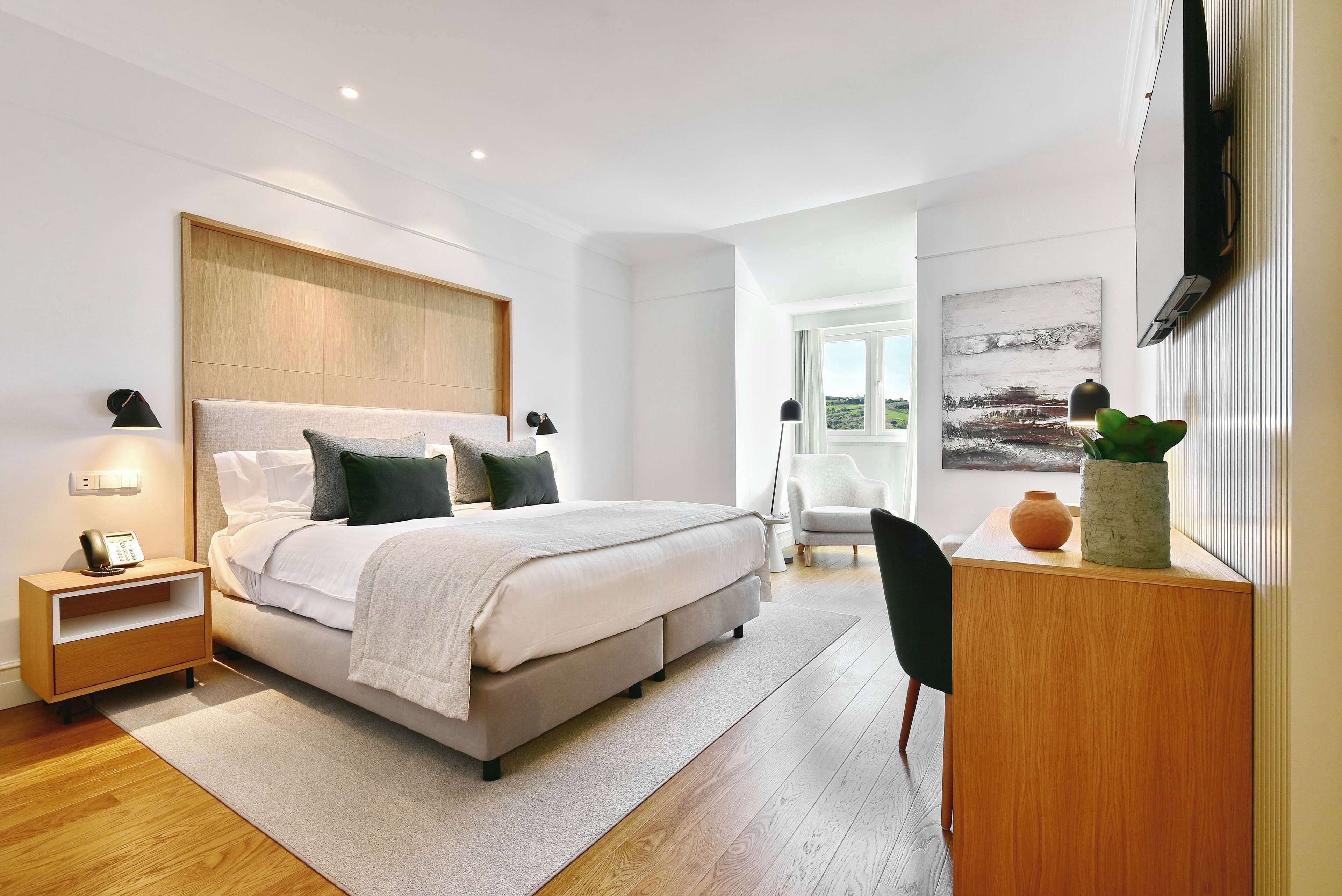 Een moderne slaapkamer met een bed, nachtkastje, lamp en uitzicht op de omgeving.