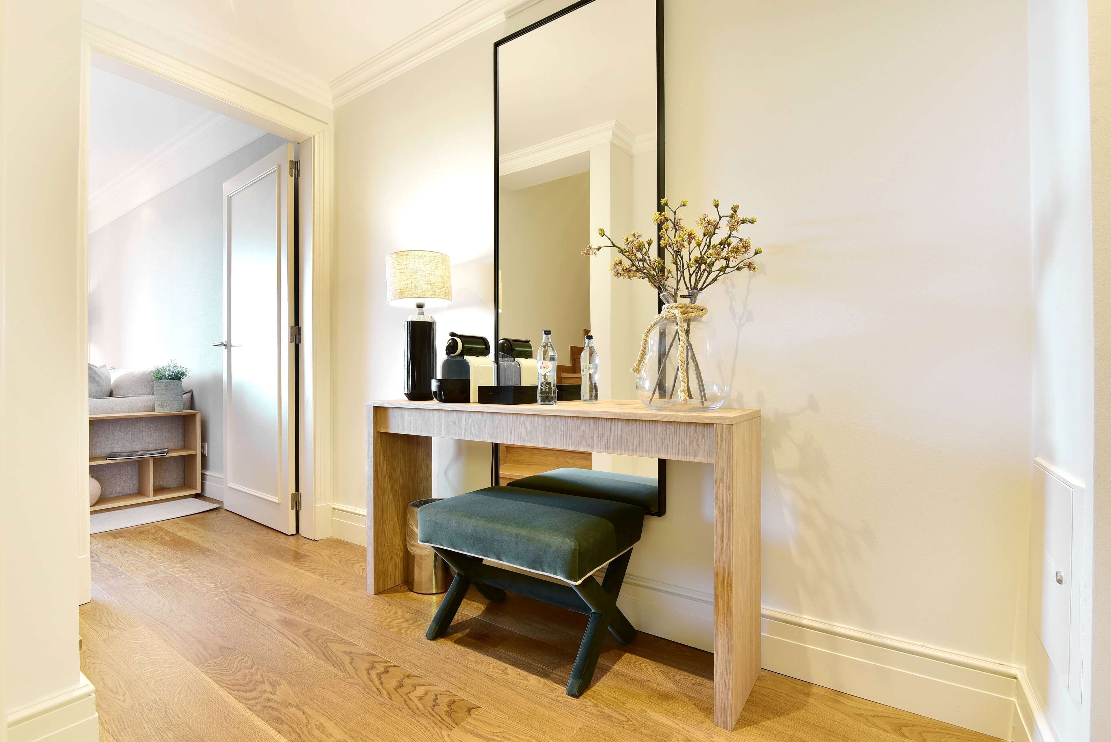 A modern bathroom with a wooden vanity, a large mirror, a green bench, and a vase with flowers.