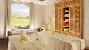 Relax in a serene room with a green landscape view, featuring a massage table, wardrobe, and seating area.