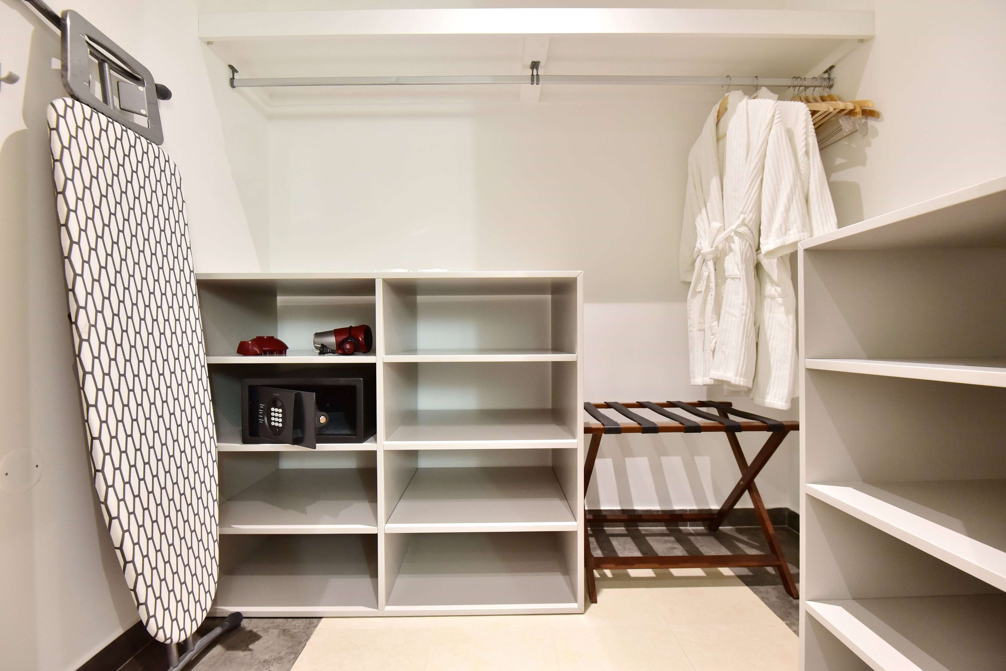 A neatly organized walk-in closet with open shelving, a hanging rack, and a patterned ironing board.