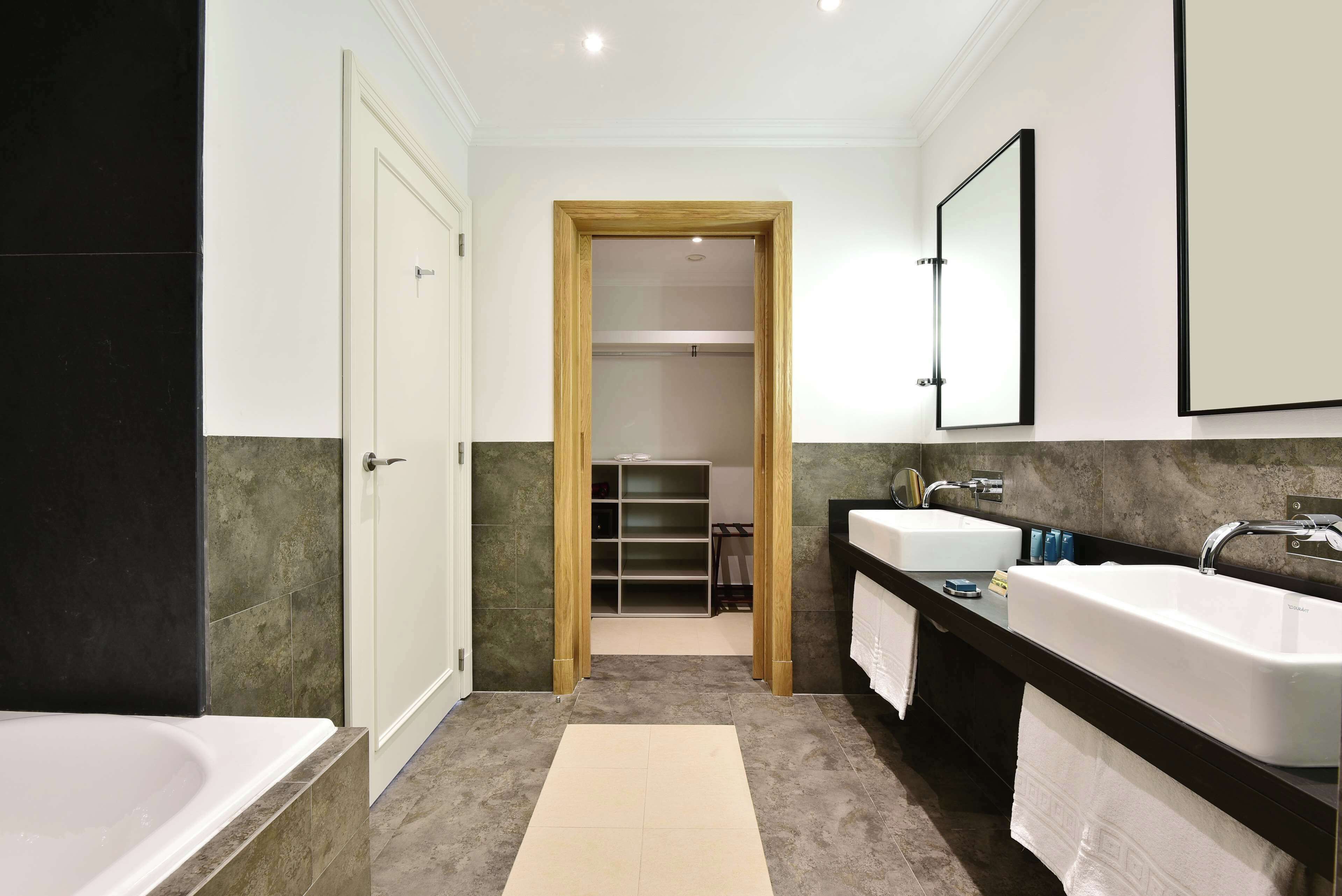 A modern bathroom with two sinks, a bathtub, and a walk-in closet.