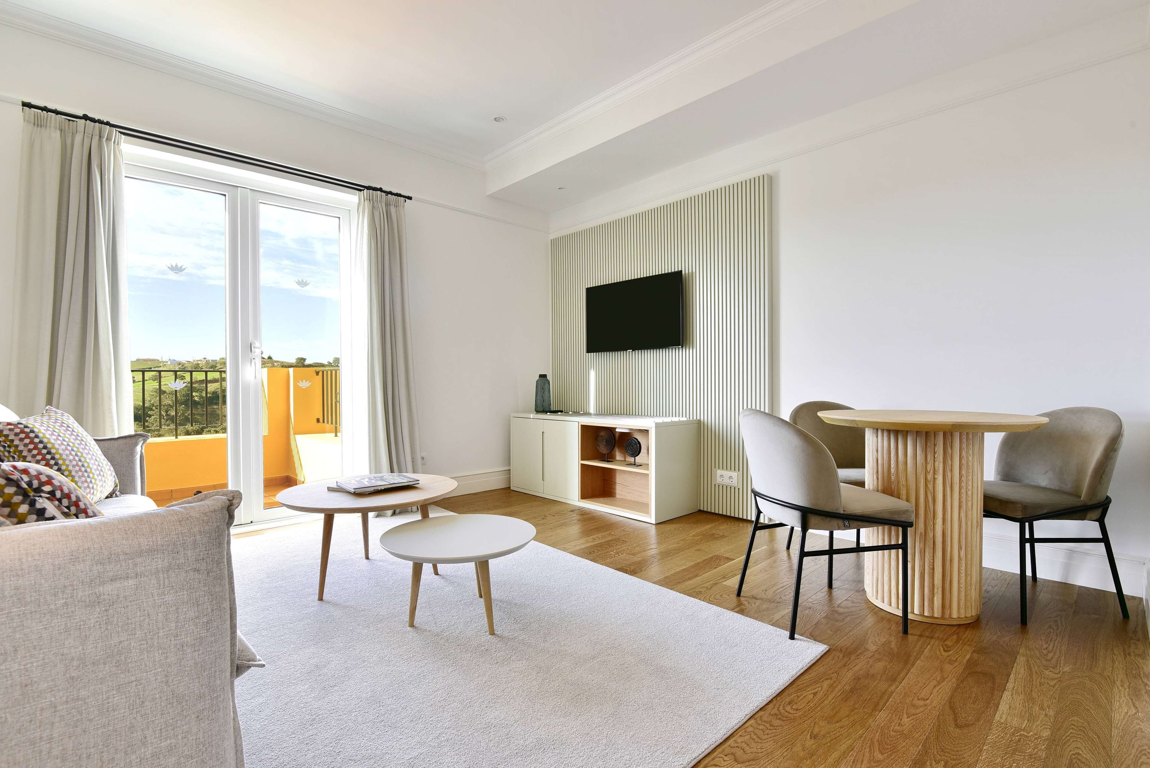Een moderne woonkamer met een bank, een rond salontafel, een aan de muur bevestigde televisie en een eethoek met stoelen en een tafel.