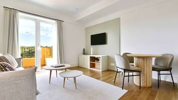 Una sala moderna con un sofá, una mesa redonda para café, un televisor montado en la pared y un comedor con sillas y una mesa.