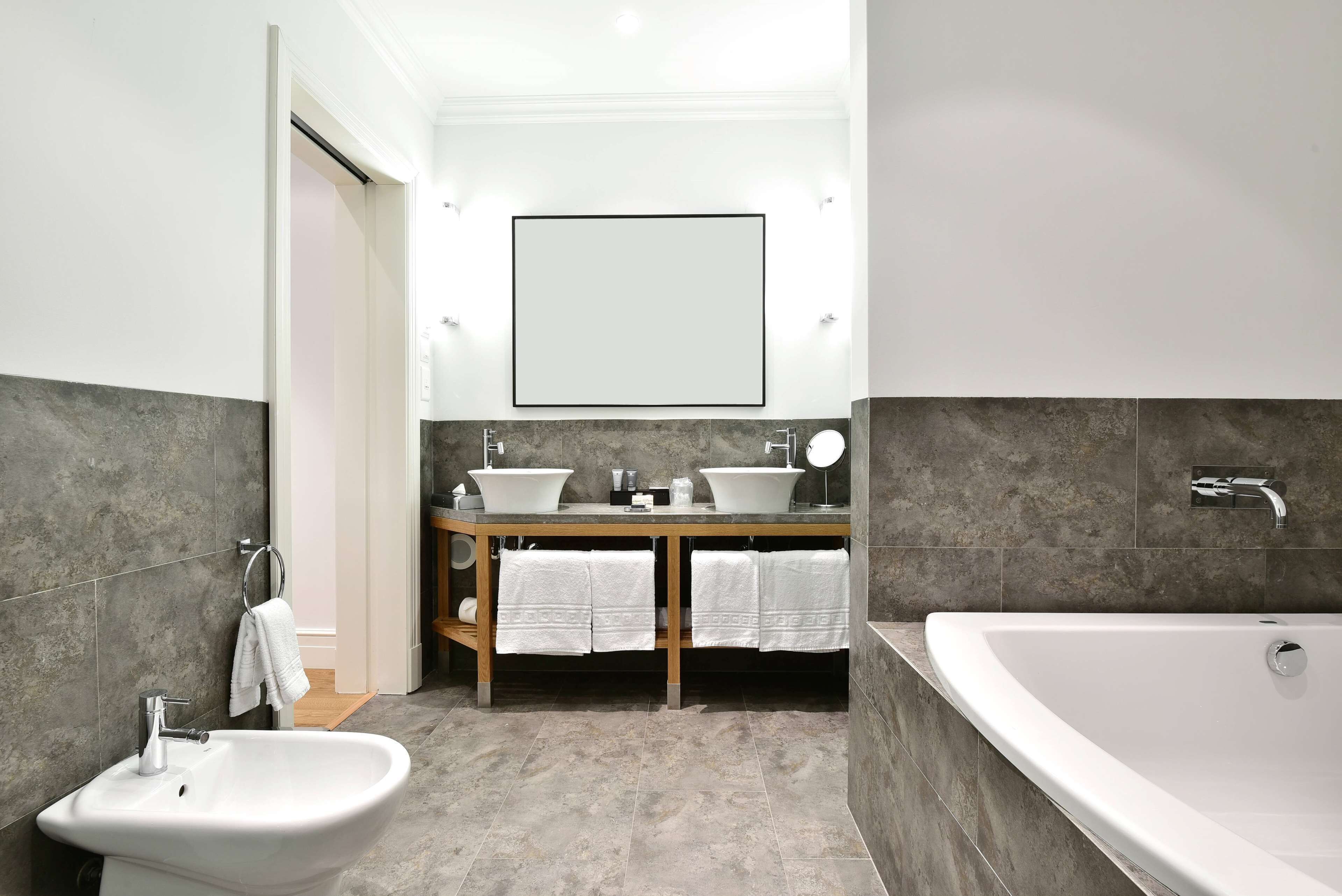 A modern bathroom with a bidet, two sinks, a large mirror, and a bathtub.