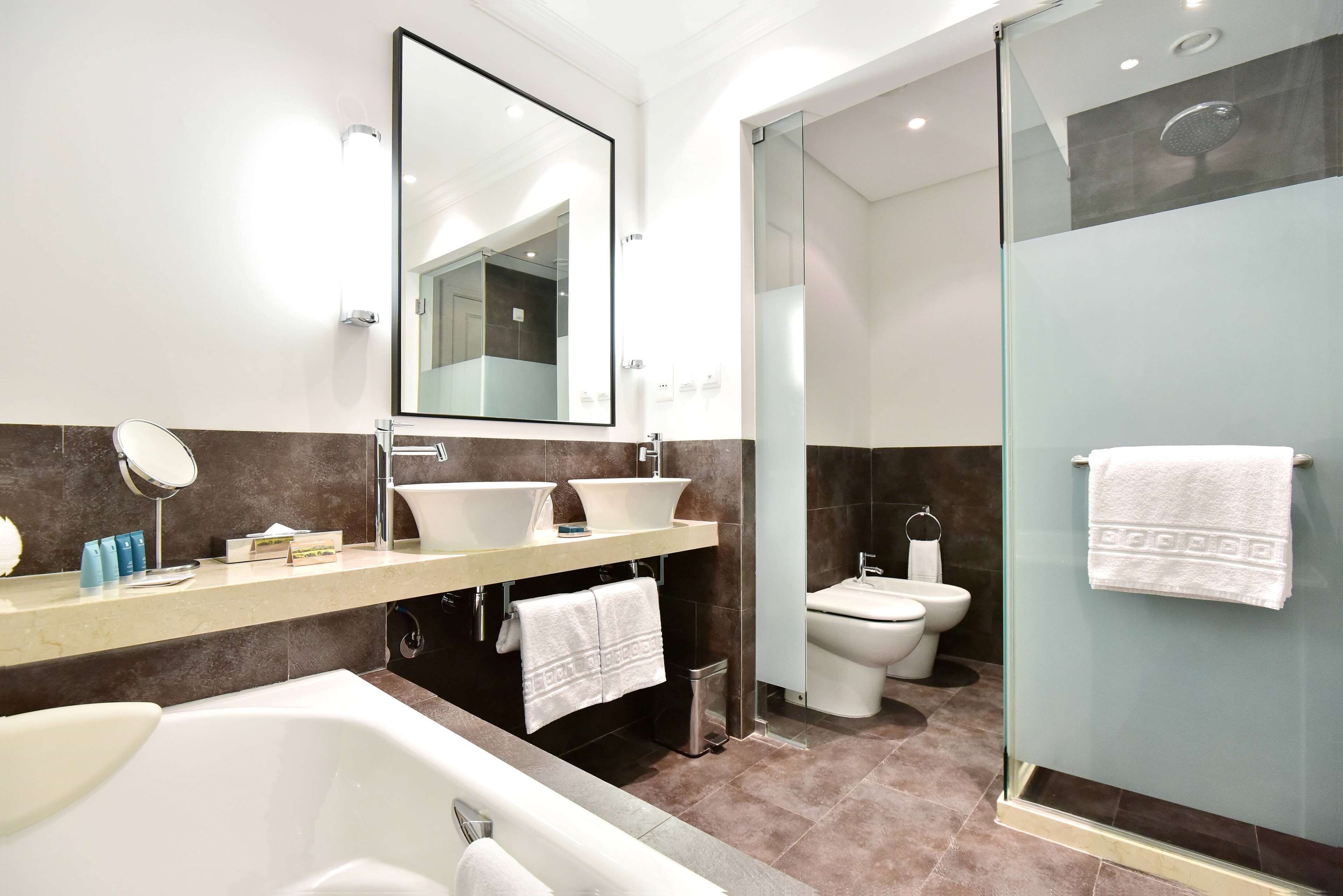 Un baño moderno con bañera, dos lavamanos, inodoro y ducha con mampara de vidrio.