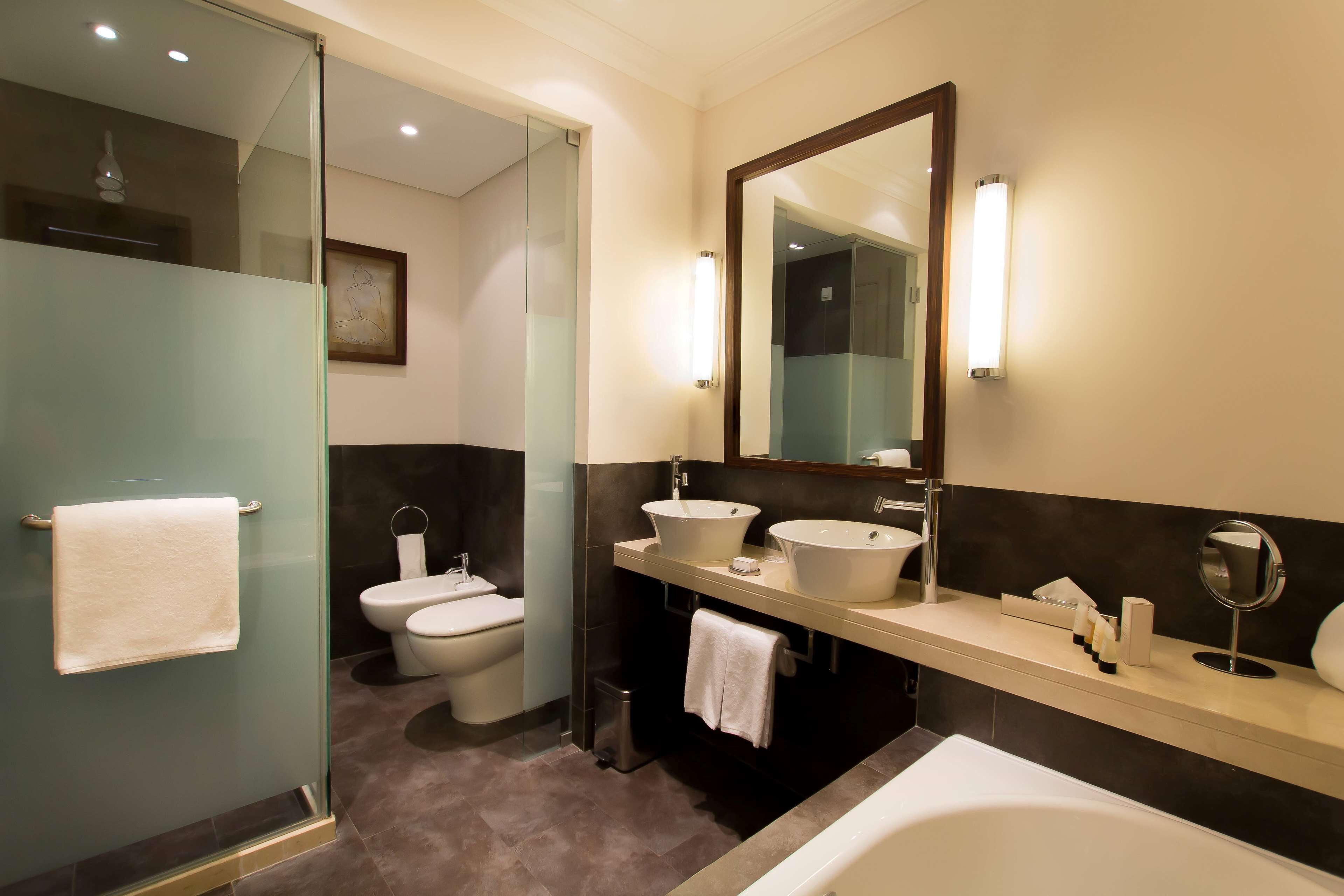 A modern bathroom with a glass shower enclosure, two sinks, a large mirror, and a bathtub.