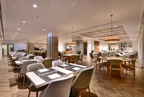 A modern dining area with multiple tables and chairs, wooden flooring, and pendant lighting. - Dolce by Wyndham CampoReal Lisboa (Torres Vedras)