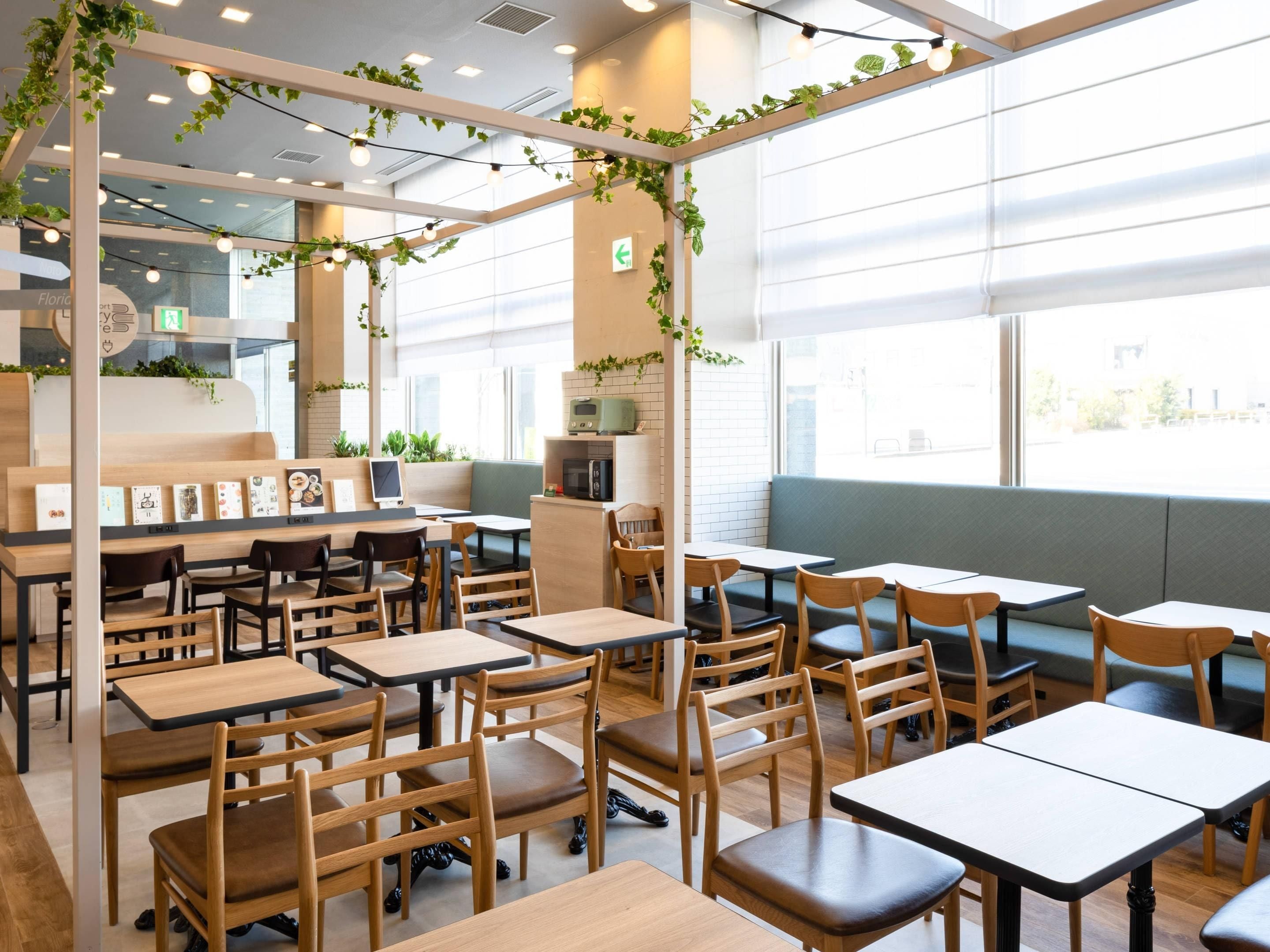 A modern cafe with wooden tables and chairs, a green wall with plants, and a bright interior.