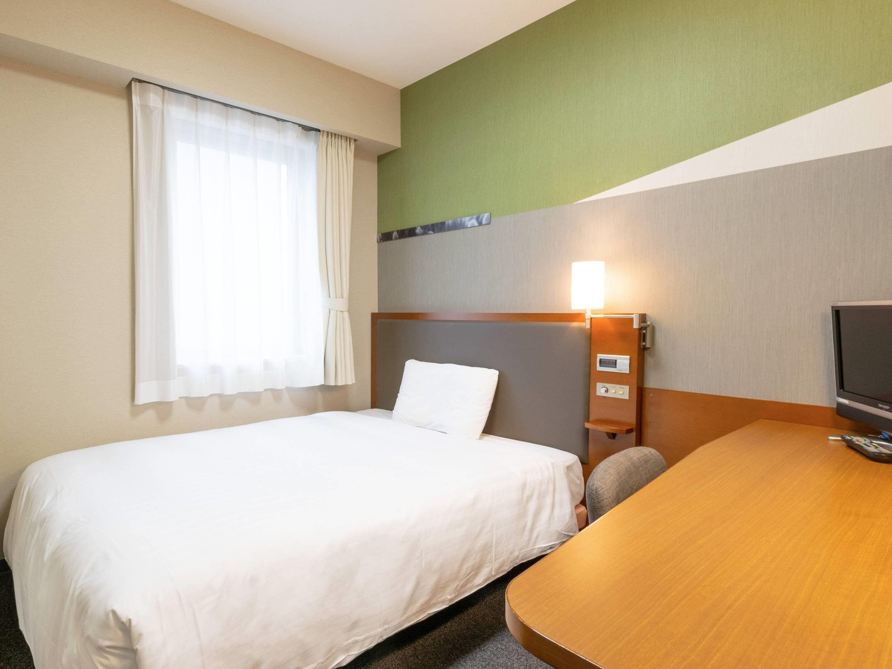 Een hotelkamer met een eenpersoonsbed, een bureau met stoel, een televisie en een wandlamp.