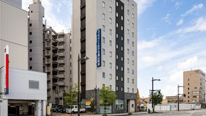 A multi-story hotel with a modern design, featuring a prominent vertical sign with Japanese characters, a parking area, and a street view with other buildings and vehicles. - Comfort Hotel Toyama (Toyama)