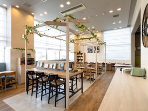 Un café moderno con mesas y sillas de madera, pared de ladrillo y un ventanal grande.