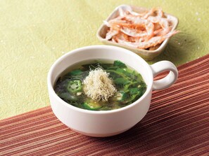 A bowl of soup with green vegetables and a white cup on a textured surface. - Comfort Hotel Toyama (Toyama)