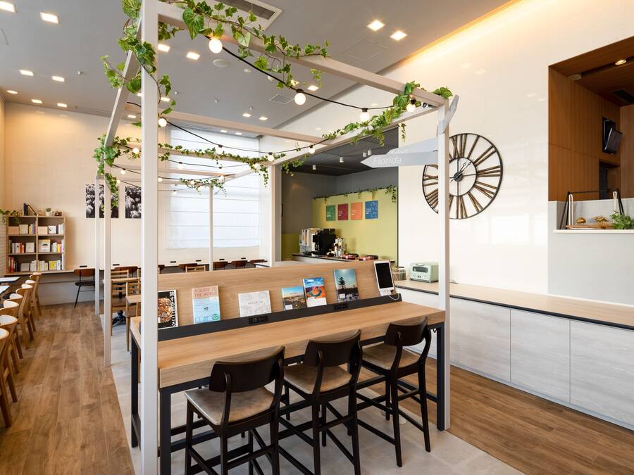 A modern cafe with wooden tables and chairs, a counter with a menu, and a wall clock.