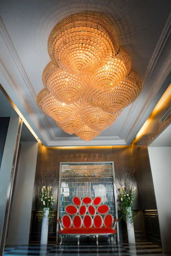 Un vestíbulo con una gran araña ornamentada, una zona de estar en rojo y blanco, y una pared decorativa con elementos verticales.