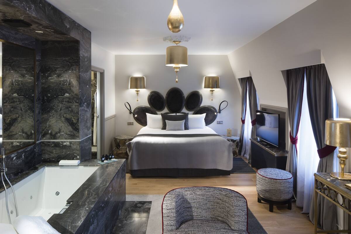 A modern bedroom with a large bed, a bathtub, and a television.