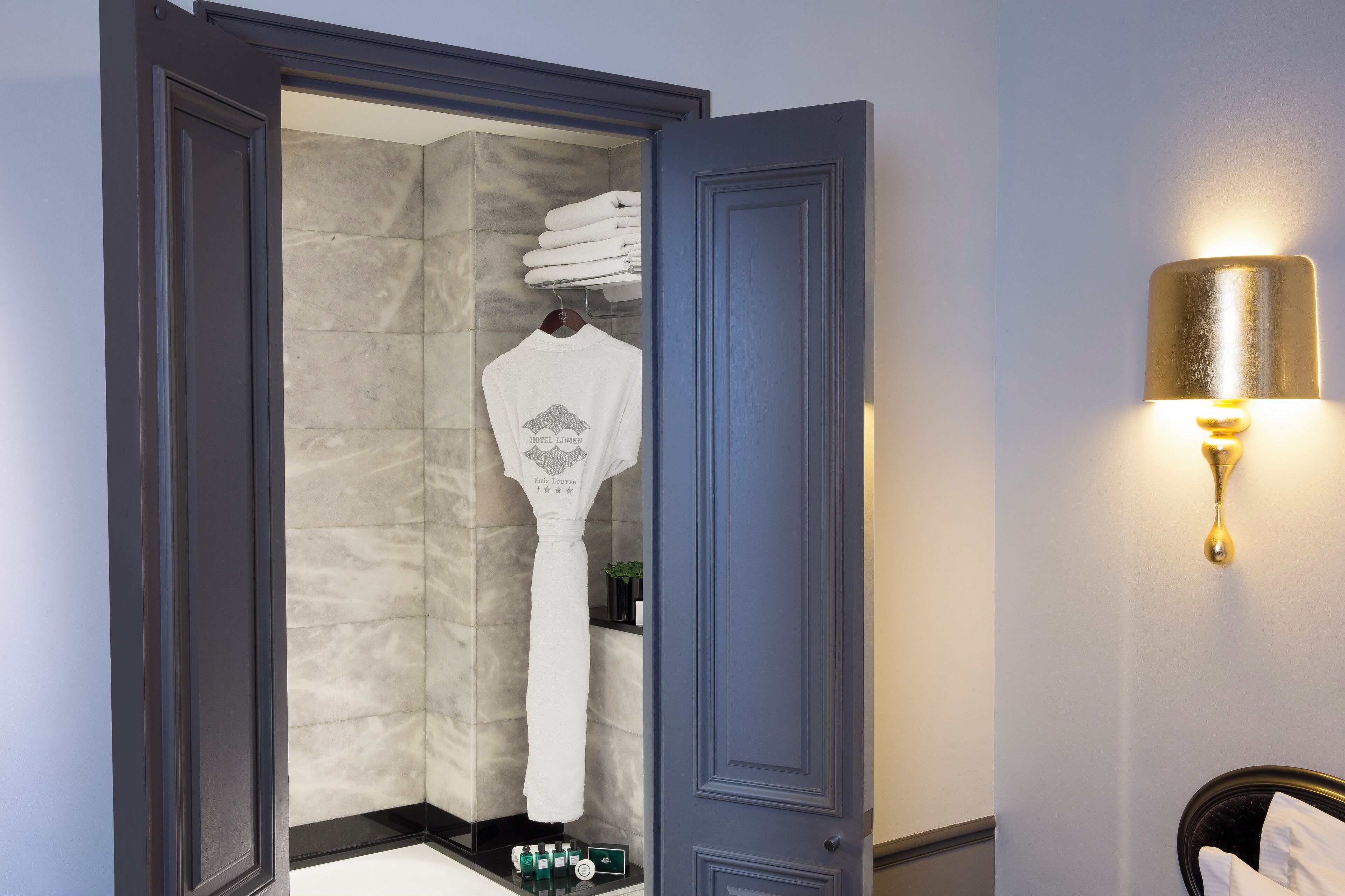Un baño con zona de ducha, un perchero con toallas dobladas y un aplique de luz.