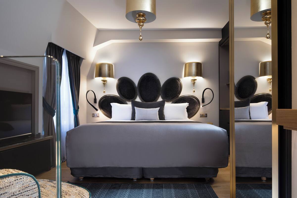 A modern hotel room with a large bed, a flat-screen TV, and a mirror reflecting the room.