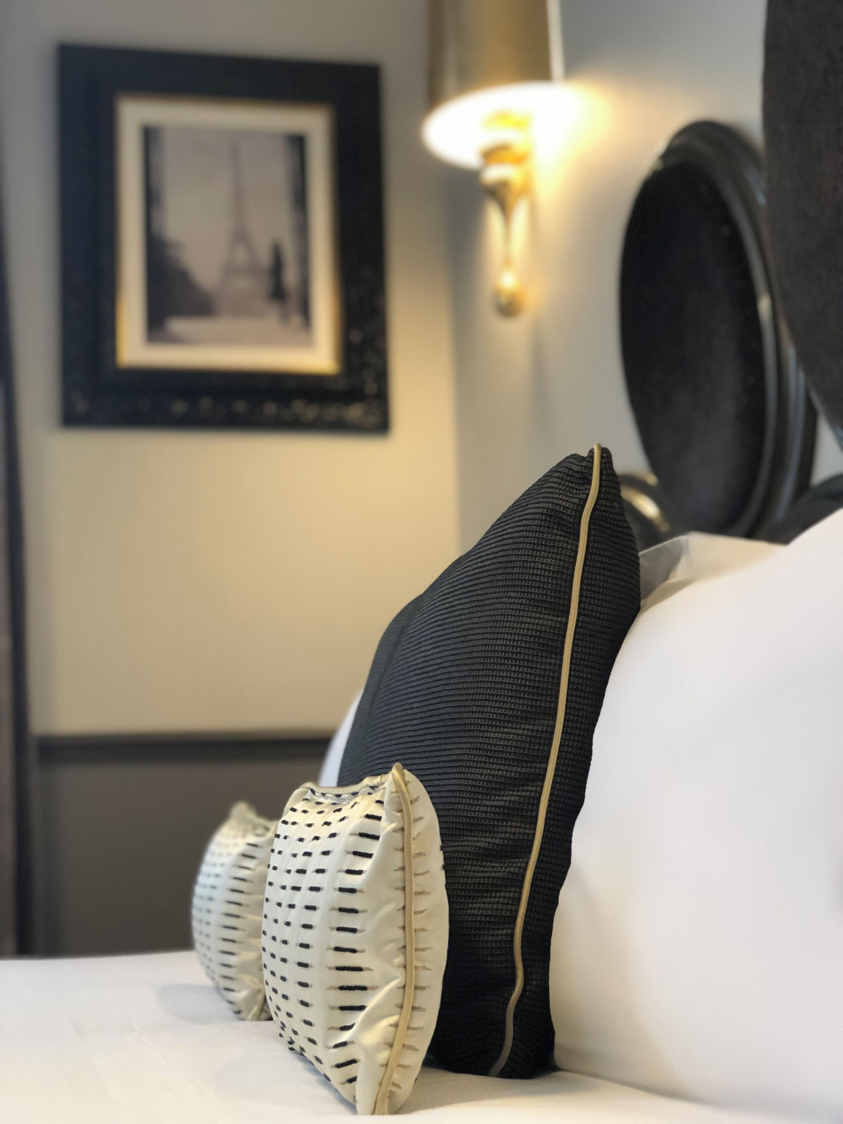 Una cama bien hecha con dos almohadas y un cojín decorativo, un cuadro en la pared y una lámpara de pared.