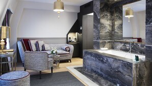 Una sala de estar moderna con una pared de acento de mármol, un espejo grande y un espacio de estar con sofá y sillón.