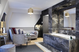 A modern living room with a marble accent wall, a large mirror, and a seating area with a sofa and armchair.