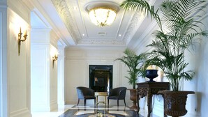 Un amplio pasillo con suelo de mármol, dos sillones, una mesa y una planta grande en maceta.