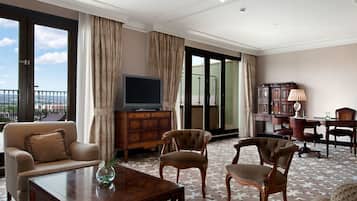 Una habitación de hotel con sofá, sillones, televisor, aparador y escritorio.
