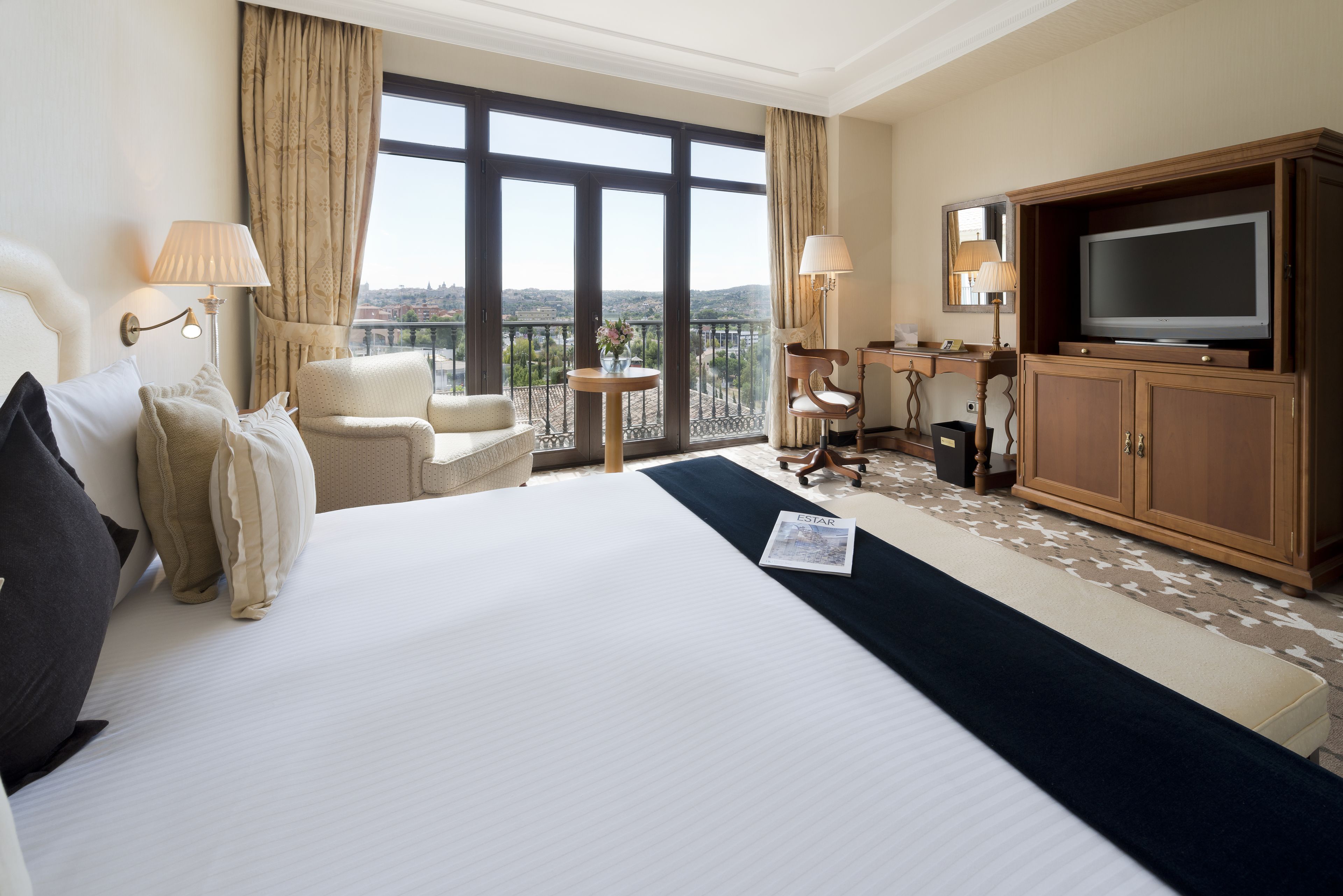 Une chambre d’hôtel dotée d’un grand lit, d’une télévision, d’un bureau avec une chaise et offrant une vue sur la ville grâce à de grandes fenêtres.