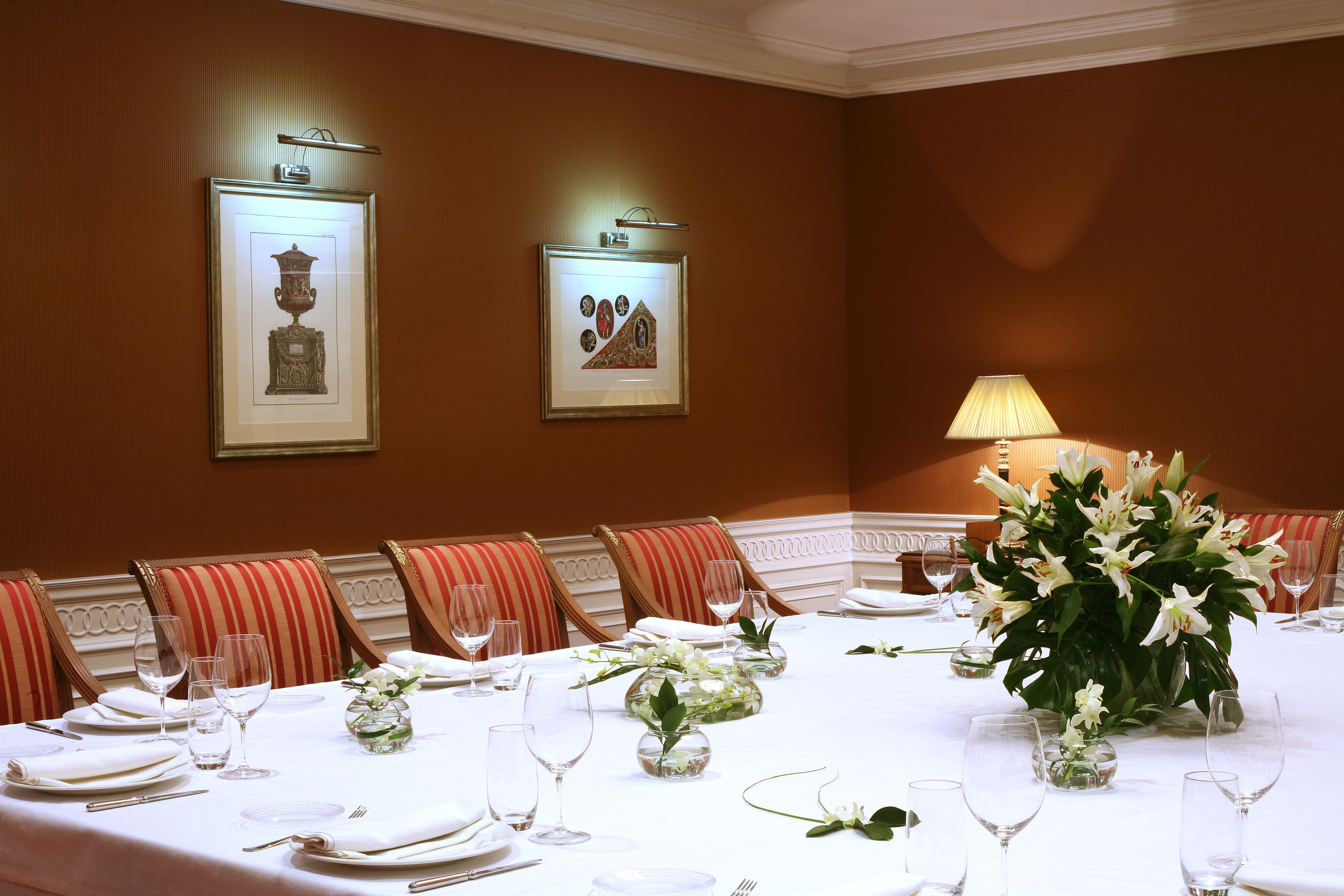 Ein formeller Speisesaal mit einem langen Tisch, der für eine Mahlzeit gedeckt ist, Kunstwerken an den Wänden und einer floralen Tischdekoration.