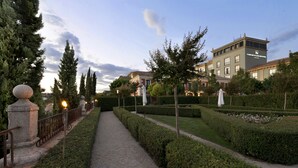 Un sendero conduce a un edificio de estilo clásico, rodeado de setos y árboles bien cuidados.
