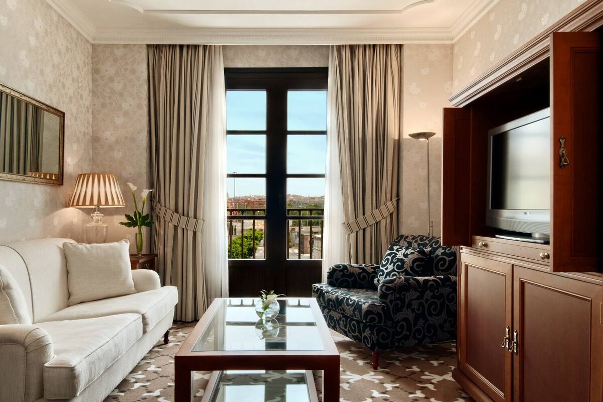 Una sala de estar con sofá, sillón, televisor y un ventanal con cortinas.